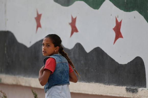 Ragazza davanti a un murales che raffigura una variante della bandiera siriana