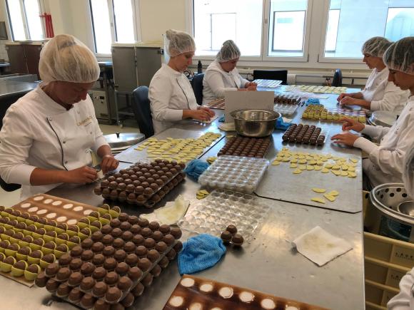 5 operaie che stanno confezionando cioccolatini di vario tipo su un lungo tavolo di lavoro.