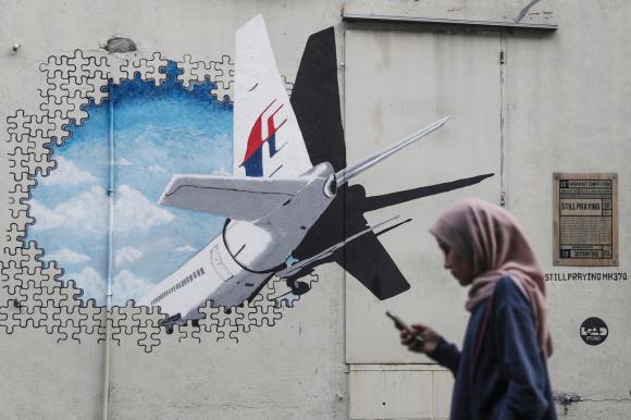 donna cammina davanti a un murales raffigurante la coda dell aereo scomparso nell oceano indiano