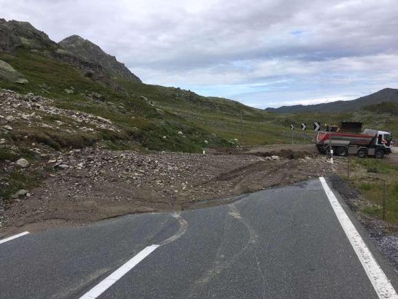 Strada di montagna interrotta da una colata di fango; camion che trasporta via i detriti sulla dx