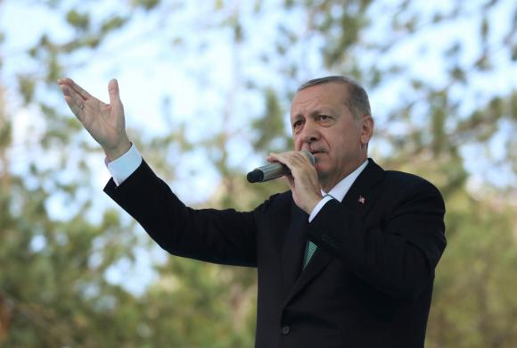 Erdogan durante un comizio, vestito in scuro con microfono in mano