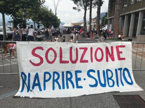 Un cartello in piazza a Campione con scritto: Soluzione, riaprire subito