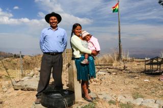 Un contadino con la moglie che tiene in braccio una bambina e sullo sfondo la bandiera boliviana