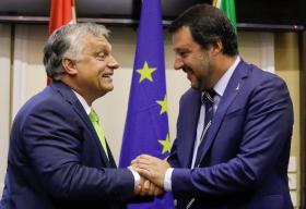 Orban e Salvini, di profilo e a mezzobusto, si stringono la mano. Sul fondo le bandiere ungherese, europea, italiana