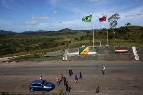 Una manciata di persone su una grossa strada asfaltata con, accanto, le bandiere di Brasile e Venezuela. Colline sul fondo