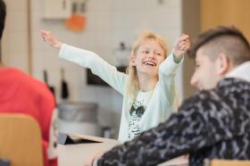 una bambina alza le braccia e ride in un aula scolastica