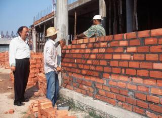 three men on a buidling site, building a wall.