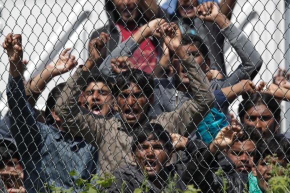Un gruppo di profughi manifestano davanti dietro alla ramina che delimita il campo profughi