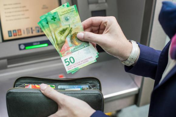 Una mano impugna 4 banconote da 50 franchi appena prelevati da un bancomat (che si vede sullo sfondo)