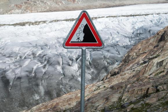 cartello con pericolo cadute massi e sullo sfondo un ghiacciaio