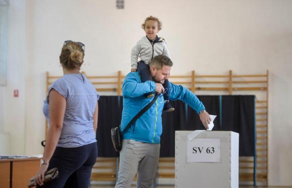 Un uomo con un bimbo sulle spalle sta votando mentre la moglie li aspetta