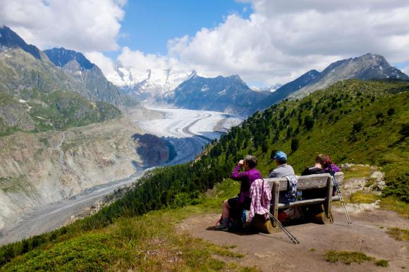 In primo piano tre escursionisti seduti sulla panchina ad ammirare il ghiacciaio dell Aletsch sullo sfondo