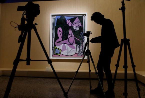 Un quadro di Picasso (Nuda con mazzo di iris e specchio) sullo sfondo e in primo piano un videomaker