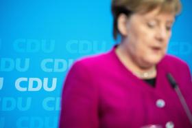 Primissimo piano sfocato di Angela Merkel, al pulpito, col logo della CDU alle sue spalle