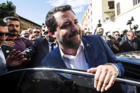 Primo piano di Salvini mentre sale a bordo di un automobile, con una mano sulla portiera; persone con foto e videocamere attorno
