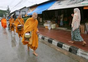 Monaci buddisti camminano su una strada, accanto a loro una donna musulmana sul marciapiede.