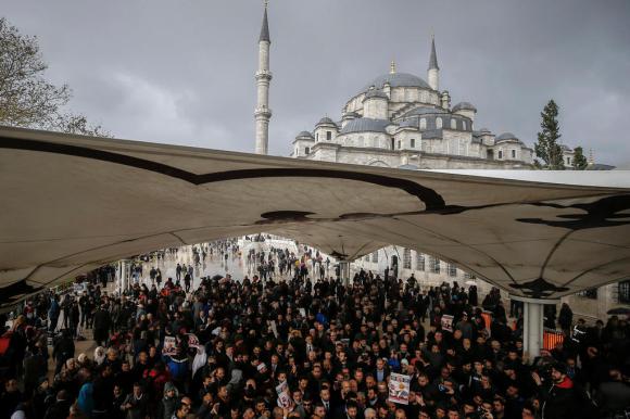 Folla di centinaia di persone, qualcuna con in mano un poster, riunita sotto un tendone nei pressi di una moschea