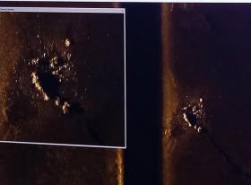 Immagine molto scura di un fondale marino; si intravvede un oggetto; sulla sx riquadro di ingrandimento