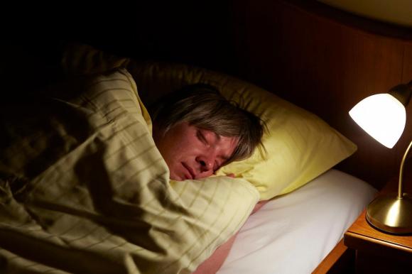 Un giovane uomo mentre dorme a letto con la lampada del comodino accesa
