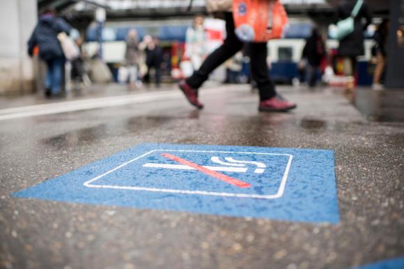 Primo piano di un simbolo vietato fumare sul pavimento di una stazione; attorno, sfocate, persone che camminano