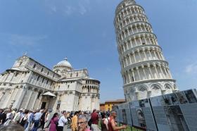 Vista della torre e del Duomo di Pisa, con decine di turisti che si dirigono verso il monumento o leggono pannelli esplicativi