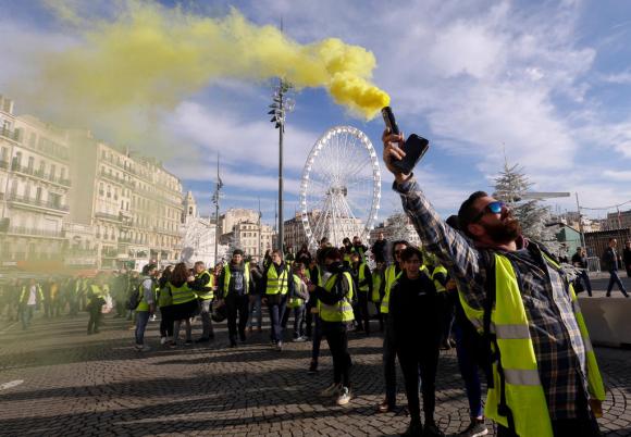 Diversi manifestanti con il gilet giallo in piazza a Parigi. In pirmo piano un uomo con gilet giallo e un fumogeno giallo