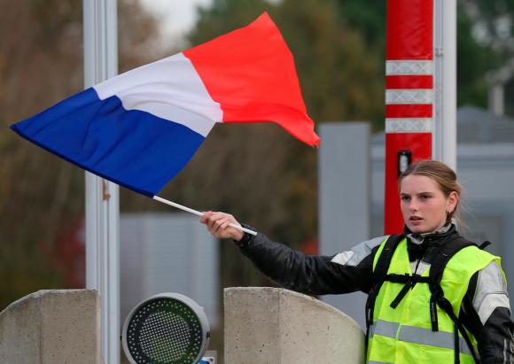 Una ragazza con il gilet giallo mentre sventola una bandiera francese ai bordi di un casello autostradale