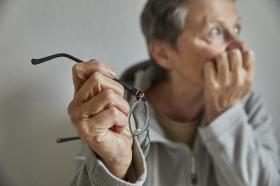 Una persona anziana tiene una mano sul mento in gesto di preoccupazione; nell altra, regge gli occhiali; volto sfocato
