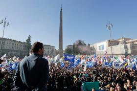 Salvini visto di spalle; di fronte a lui piazza del popolo a Roma piena di gente e di bandiere che inneggiano alla Lega