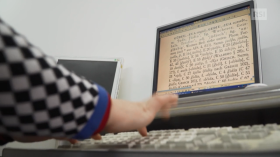 Mani che scrivono sulla tastiera d un computer; a fuoco lo schermo, sul quale si distingue il testo d un dizionario