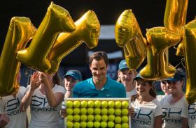 Roger Federer regge un quadro fatto di palline da tennis, attorniato da ragazze che indossano cappellino da tennista