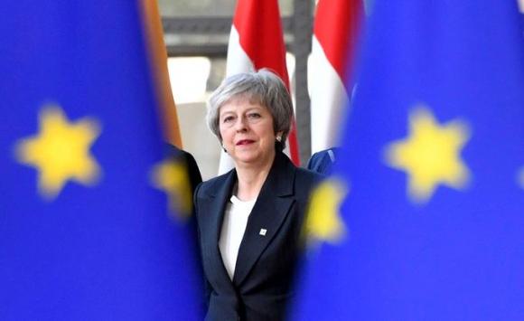 Theresa May davanti a due bandiere europee