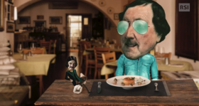 Figura di Rossini con occhiali da sole e camicia di jeans al tavolo di un osteria, sul quale campeggia un personaggio stile gnom