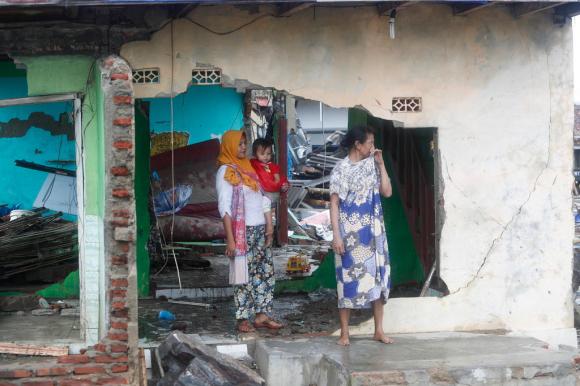 Immagine di una casa parzialmente sventrata, con detriti all interno; due donne e un bambino sulla soglia