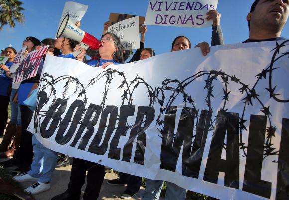 Manifestanti con uno striscione con scritto Border Wall attorniato da filo spinato