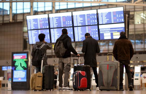 Quattro viaggiatori all aeroporto di Amburgo che guardano sul tabellone i voli cancellati
