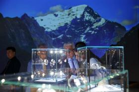 Visitatori ammirano orologi esposti all interno di due teche; alle loro spalle immagini delle Alpi