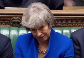 Primissimo piano di Theresa May con blazer blu, seduta alla Camera dei Comuni