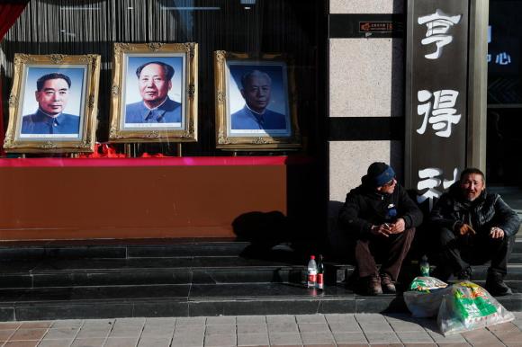 Due operai cinesi seduti accanto ai ritratti di tre leader cinesi: Mao Zedong, Zhou Enlai e Liu Shaoqi in una piazza a Pechino