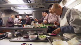 Jeong Kwan in una cucina professionale con una brigata; posa con cura delle verdure su un piatto