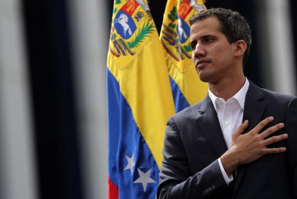 Juan Guaidò, mano destra sul cuore, bandiera venezualana dietro le spalle, ritratto dopo l autoproclamazione a presidente