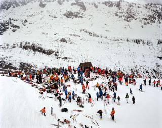 Assembramento di persone in tuta da sci e con gli sci sul cucuzzolo di una montagna innevata