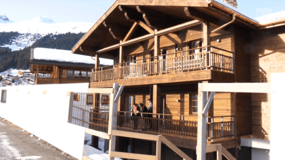 Immagine di un abitazione di montagna costruita in gran parte in legno; potenziali acquirenti la visitano;paesaggio innevato