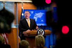 Il segretario di Stato Pompeo parla da un pulpito accanto a una bandiera USA e un monitor con la mappa del mondo