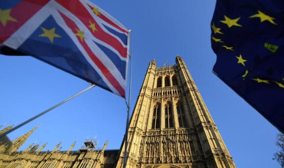 Vista dal basso di una torre di Westminster con, in primo piano, parti di una bandiera UE e una britannica con stelle
