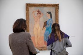 Due donne di schiena guardano un quadro raffigurante due donne, di cui una nuda, in cornice dorata