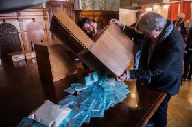 Due persone rovesciano le schede di voto contenute in un urna su un tavolo per il conteggio.