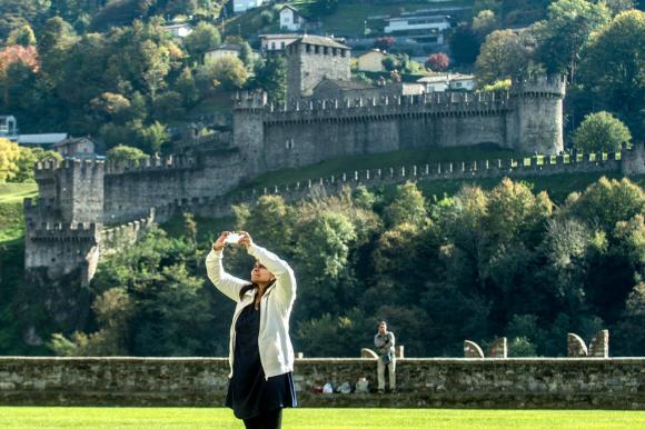una donna sta scattando una fotografia, alle sue spalle si vede il castello di Montebello di Bellinzona.