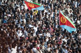 Vista dall alto di una folla di persone intenta a manifestare; sventolano due grosse bandiere eritree