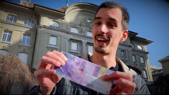 Bild eines jungen Mannes vor der Nationalbank mit einer 1000er-Note in den Händen.